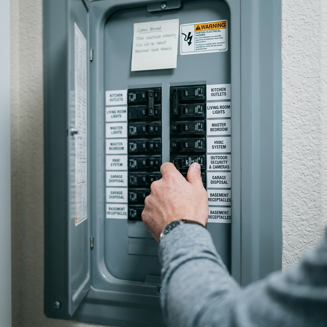 Person manually flipping an outdoor security circuit breaker to the OFF position inside a modern home fuse box